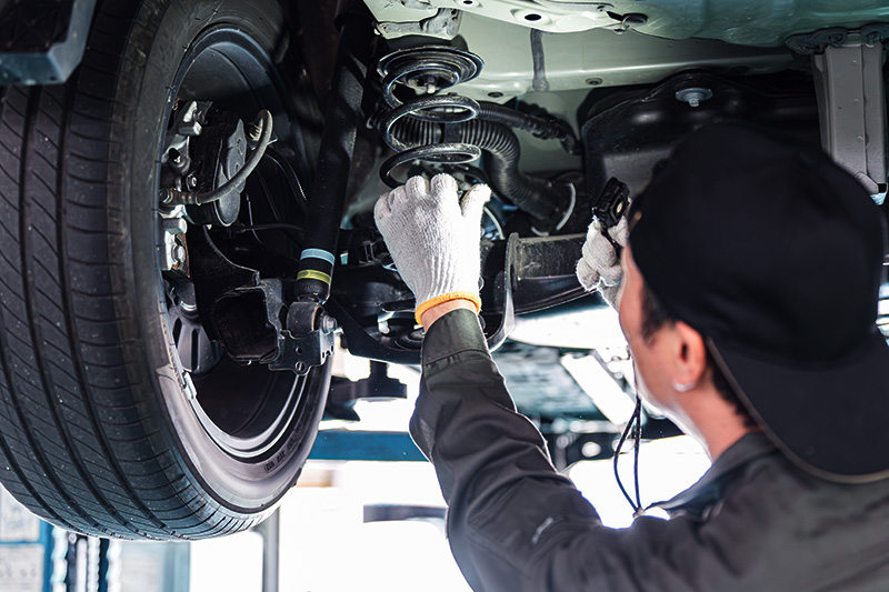 Auto technician inspecting suspension and steering components under vehicle