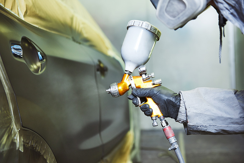 Auto technician spray painting vehicle during auto body repair